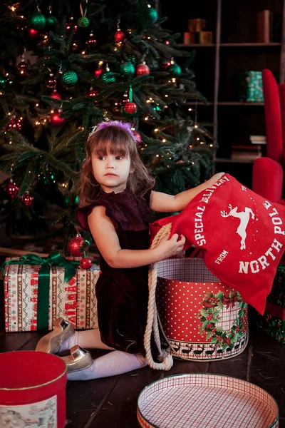 Menina sorridente feliz com caixa de presente de Natal sentado no chão perto de uma árvore de xtmas — Fotografia de Stock