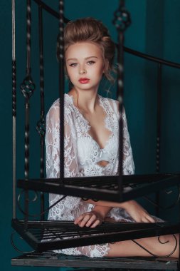 Beyaz sabahlık siyah Dövme demir merdivenlerde oturan güzel sarışın gelin.