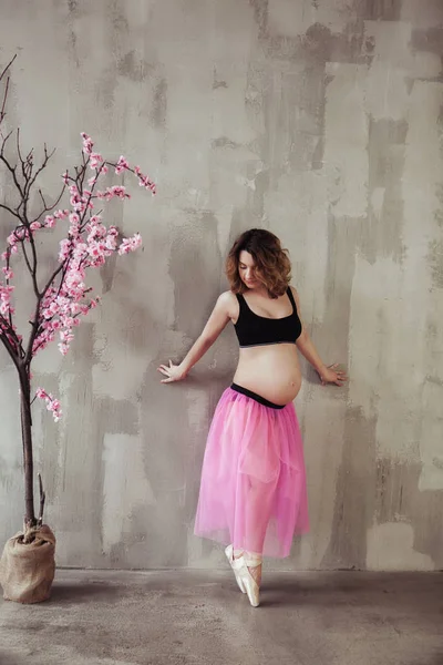 Schwangerschaft Fitness und Sportkonzept glücklich schwangere Frau in der Nähe des rosa Sakura-Baums. Balletttänzer auf grauem Hintergrund. Dachgeschossausstattung — Stockfoto