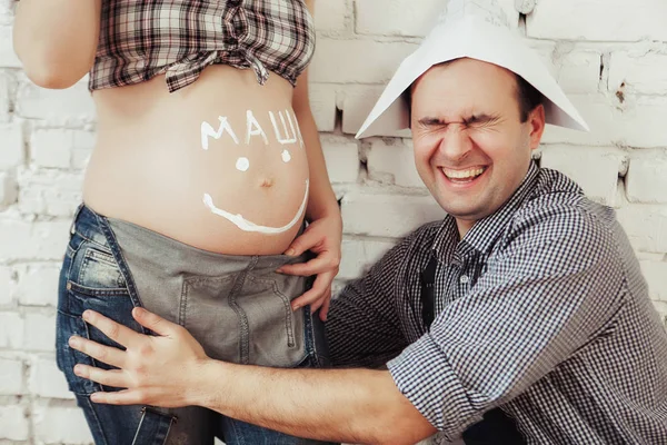젊은 남자 그의 임신한 아내의 뱃속에 행복 하 게 웃는 얼굴을 그립니다. 사랑과 행복에 대 한 개념 — 스톡 사진