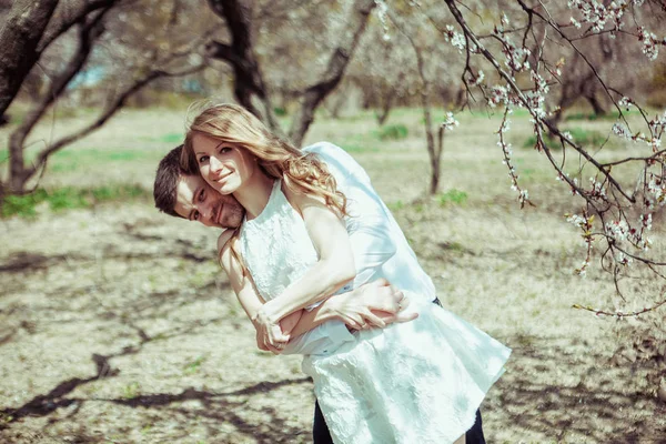 Joven pareja feliz enamorada al aire libre. hombre y mujer cariñosos en un paseo en el parque floreciente de primavera —  Fotos de Stock