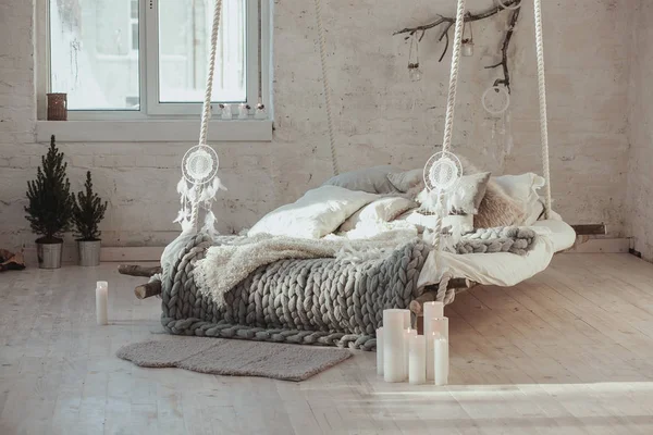 The bed suspended from the ceiling. Grey big cozy blanket knit. Scandinavian style, gray plaid, candles.