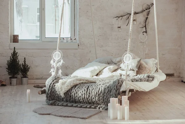 The bed suspended from the ceiling. Grey big cozy blanket knit. Scandinavian style, gray plaid, candles. — Stock Photo, Image