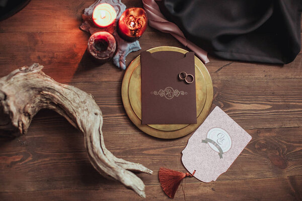Graphic arts of beautiful wedding pink and brown cards, golden plate with two rings, candles, fabric, snag on wood background. Top view