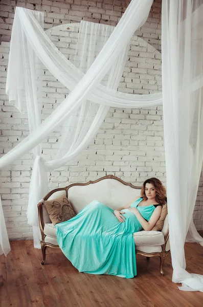 Hermosa mujer embarazada en vestido azul relajante en el sofá — Foto de Stock