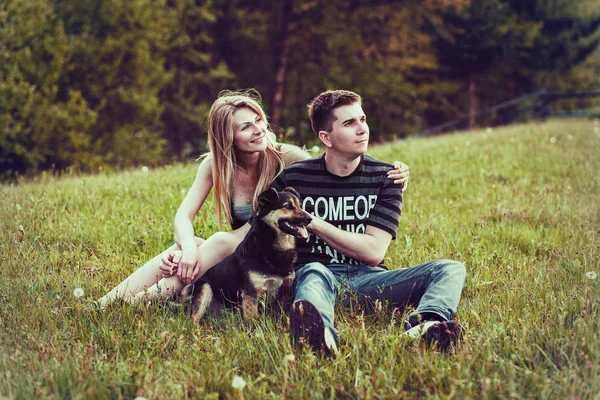 Couple with a dog sitting on the grass in the forest — Stock Photo, Image