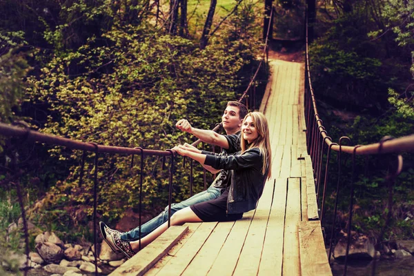 Happy couple sitting on the bridge in a forest — Stock Photo, Image