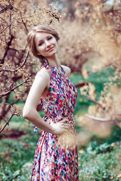 Portret van een jonge blonde vrouw in een roze jurk op een achtergrond van bloeiende bomen — Stockfoto
