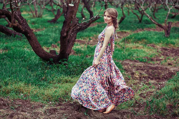 Ritratto di una giovane donna bionda su uno sfondo di alberi in fiore. Una ragazza che gira. abito rosa svolazzante nel vento — Foto Stock