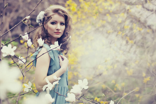 Beautiful blonde with beautiful hairstyle in vintage blue dress in a lush spring garden magnolia.