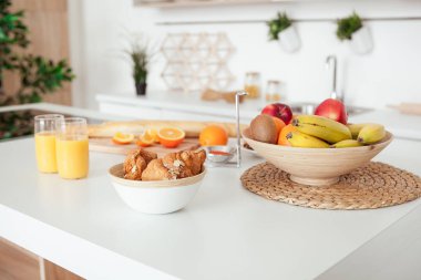 Lezzetli çerezler çikolata kırıntıları, kruvasan, baget, muz, elma, Trabzon hurması, turuncu ve portakal suyu beyaz masaya tabak