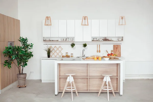 Interior de la pequeña cocina blanca con fruta fresca, dos vasos de jugo de naranja, baguette, caviar rojo, croissant y galletas con chispas de chocolate en la mesa — Foto de Stock