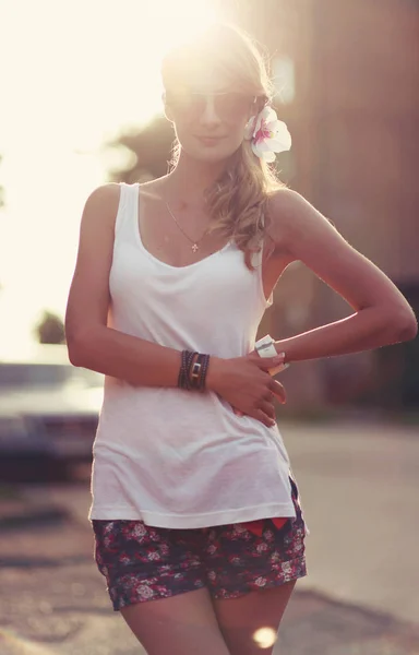 Mooie jonge blonde vrouw staande op het strand. Het dragen van witte T-shirt. Wind waait in haar lange blonde haren. In de achtergrond is zonsondergang en warm gevoel — Stockfoto