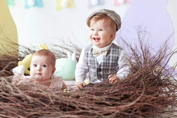 Bonito criancinhas, menino e menina, brincando com ovos de páscoa, sentados em ninho artesanal, conceito de infância felicidade Páscoa — Fotografia de Stock