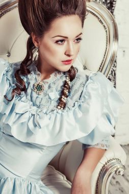 Kapalı Marie Antoinette tarzda vurdu. Bir genç seksi elbiseli kız yemyeşil mavi retro yüksek bir saç modeli ile kanepede oturuyor. Kadın lüks yorgun