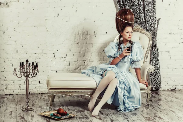在室内拍摄的玛丽 · 安托瓦内风格。郁郁葱葱的蓝色复古裙与高发型年轻性感的女孩坐在沙发上。厌倦了豪华的女人 — 图库照片