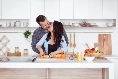 Bir kaç taze organik meyve suyu mutfakta birlikte yapma. Genç bir kadın mavi gömlekli bir baget dilimler. Bir adam kız arkadaşı bir beyaz mutfak sarılıyor. Romantik kavramı
