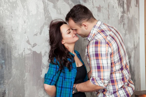 Portrait of beautiful young couple in casual clothes hugging and smiling, standing against gray wall — Stock Photo, Image