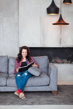 Genç kadın evde rahatlatıcı. Bir rahat tarzı güzel kızı koltukta oturur ve loft tarzı ev adlı bir kitap okur