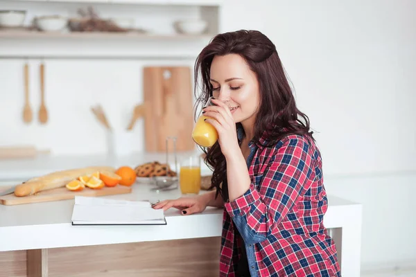 Café da manhã - Livro de leitura de mulher sorridente na cozinha branca, suco de laranja fresco — Fotografia de Stock