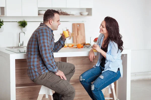 Привлекательная пара, сидящая с соком и смеющаяся дома на кухне — стоковое фото