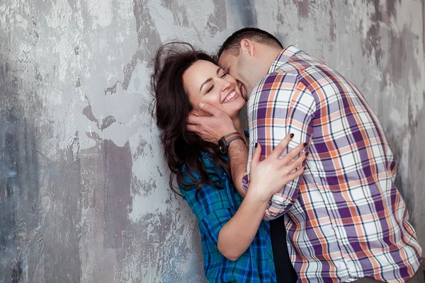 Retrato de hermosa pareja joven en ropa casual abrazando y sonriendo, de pie contra la pared gris —  Fotos de Stock