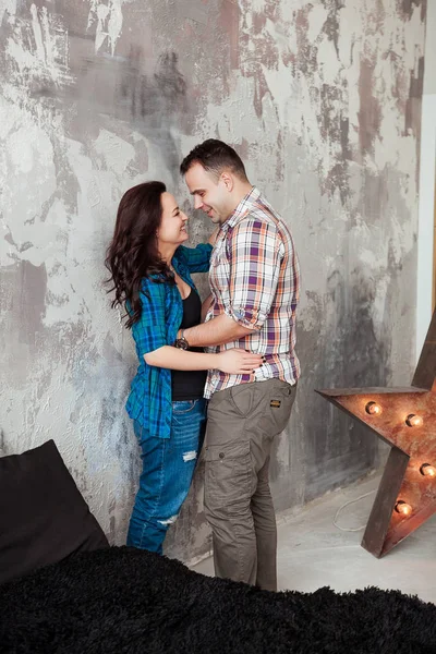 Ritratto di bella giovane coppia in abiti casual che abbraccia e sorride, in piedi contro il muro grigio — Foto Stock