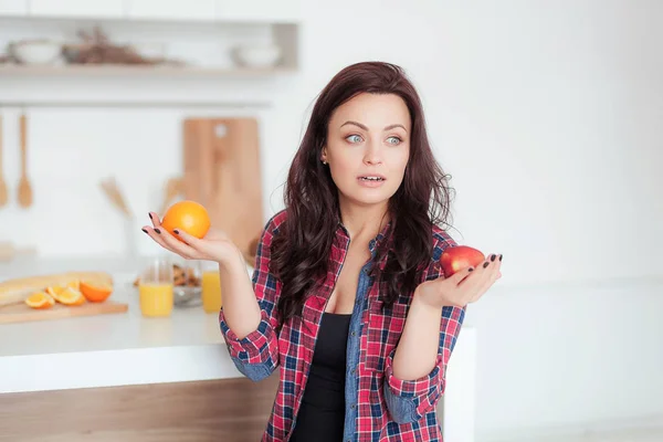 Disparo de una mujer caucásica de pelo oscuro comparando manzanas con naranjas — Foto de Stock