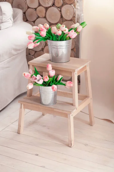 Hermosos tulipanes suaves en un cubo en un soporte de madera para flores cerca del sofá —  Fotos de Stock