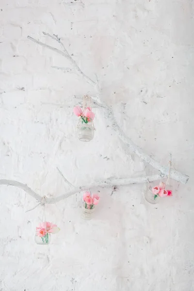 Los tulipanes en los floreros cuelgan de la rama decorativa en la pared con los ladrillos blancos —  Fotos de Stock