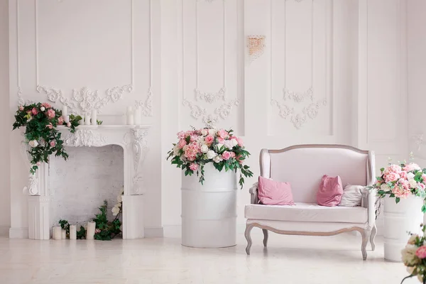 Sofá ligero con almohadas de color rosa se encuentra en la sala de estudio de luz interior cerca de la chimenea romántica decorada con flores de primavera, corona, velas —  Fotos de Stock