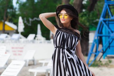 Lüks seyahat etmek siyah beyaz beachwear kum yaz sahilde yürüyüşe yürüme kadında. Kız turizm yaz tatil vacation resort adlı şapka ve sarı güneş gözlüğü güneş holding