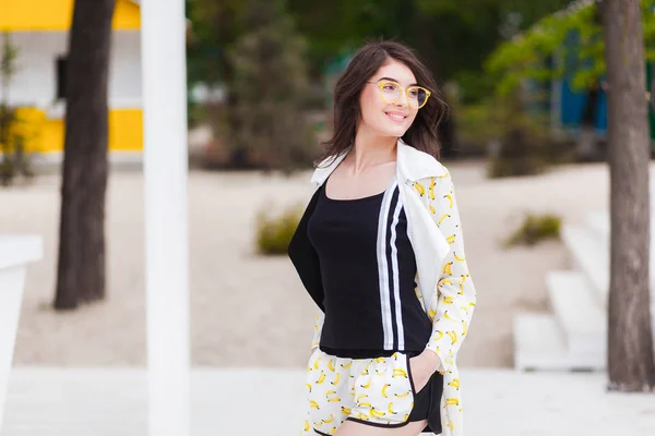 Beautiful young woman on a beach in shorts, black shirt and sunglasses — Stock Photo, Image