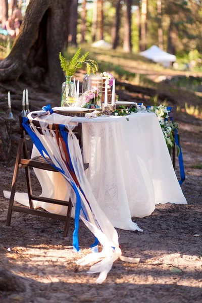 Decorazioni nuziali. Zona foto in legno situato nella foresta e decorato da tavolo, sedia, cupola di vetro, nastri e fiori . — Foto Stock