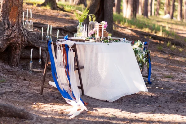 Decorazioni nuziali. Zona foto in legno situato nella foresta e decorato da tavolo, sedia, cupola di vetro, nastri e fiori . — Foto Stock