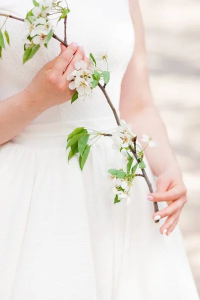 Hermosa novia chica en un vestido de encaje blanco, sosteniendo una rama con flor de cerezo — Foto de Stock