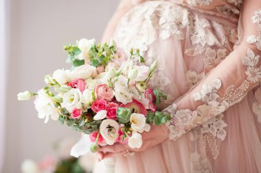 Elinde bir buket ile hamile kız bej elbise giymiş. Doğal. Bir mucize bekliyorum.