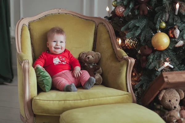 Menino vestindo pulôver vermelho sentado na poltrona vintage pela árvore de Natal — Fotografia de Stock