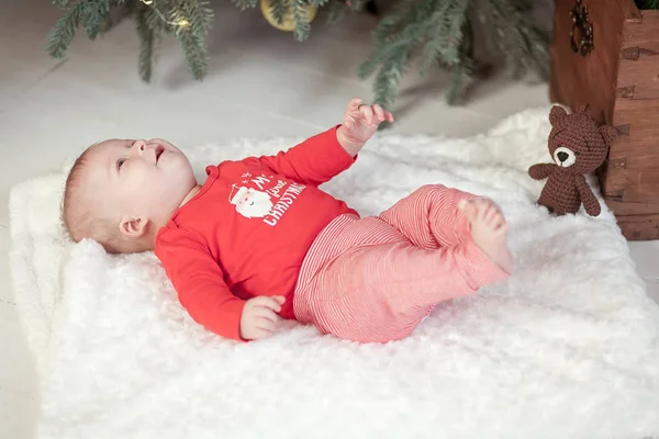 Cute newborn baby lies under christmas tree on a white fleece in red pullover close-up — Stock Photo, Image