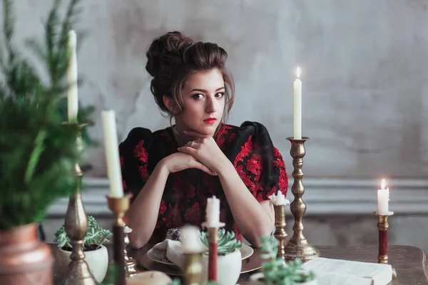 Cena de Navidad. Mujer sentada a la mesa de madera, velas blancas, decoración de adornos de abeto. Pared gris claro detrás — Foto de Stock