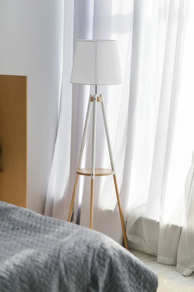 Modern interiör av ett sovrum i nya huset. Vit lampa som står på golvet nära fönstret täckt med tyll gardiner. Loft och skandinavisk design. — Stockfoto