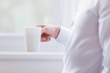 Damat veya adam bir fincan kahve elinde tutar. Beyaz pencere arka plan üzerinde