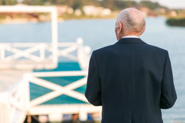 Kamera göl kenarında pier yakınındaki duran yaşlı bir adam. İş takım elbise