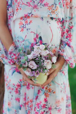 Çiçekler holding eller karnından yakınındaki içinde renkli hamile kadın kapatmak.