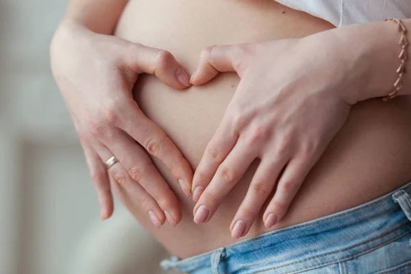 Mujer embarazada haciendo una forma de corazón con las manos sobre la barriga — Foto de Stock