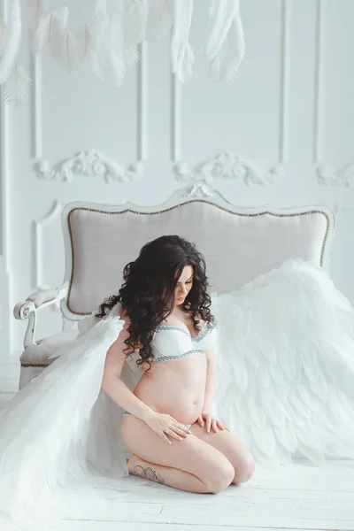 Menina grávida bonita com grandes asas de anjo no estúdio branco . — Fotografia de Stock