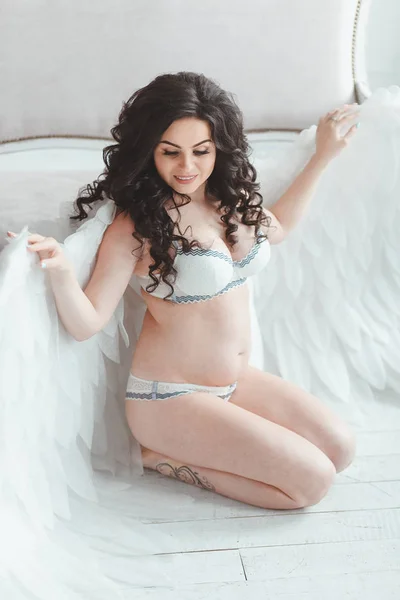 Schöne junge schwangere Mädchen mit großen Engelsflügeln im weißen Studio. — Stockfoto