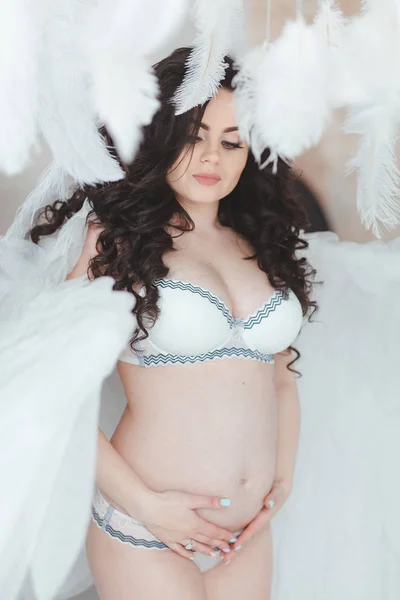 Schöne junge schwangere Mädchen mit großen Engelsflügeln im weißen Studio. — Stockfoto