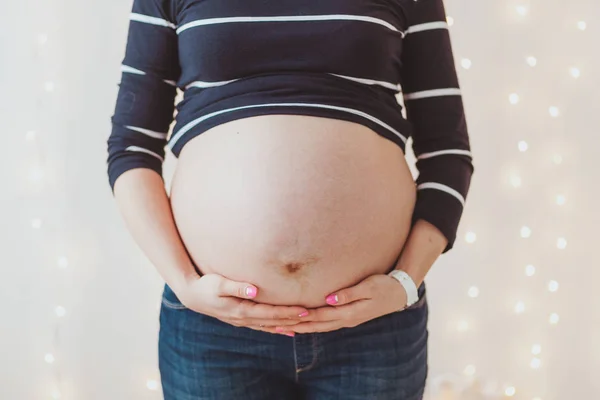 Primer plano de las mujeres embarazadas gran vientre peludo sobre fondo de luces bokeh brillante — Foto de Stock