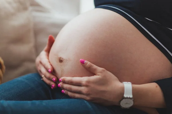 Mujer embarazada sentada en el sofá y sosteniendo su vientre de cerca — Foto de Stock